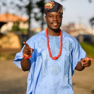 A close-up shot of a cheerful yet confused Yoruba man trying to figure something out. His lively expression blends happiness and puzzlement, capturing a lighthearted moment while he is dressed in traditional attire, reflecting both charm and cultural pride.